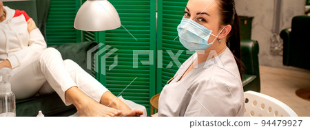 Young female podiatrist with a protective mask doing chiropody and looking at the camera in her podiatry clinic Young female podiatrist with a protective mask doing chiropody and looking at the camera in her podiatry clinic 94479927