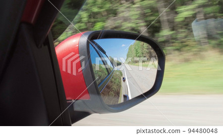 Driving a vehicle on highway at sunny day with view from side mirror. 94480048