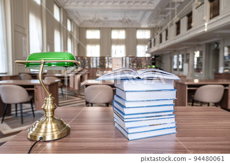 Book stack on wood desk and blurred bookshelf in the library room. Book stack on wood desk and blurred bookshelf in the library room. 94480061