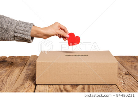 Charity. Red heart as symbol of peace, love is putting by female hand into slot of donation carton box. Concept of donorship, life saving or charity Charity. Red heart as symbol of peace, love is putting by female hand into slot of donation carton box. Concept of donorship, life saving or charity 94480231