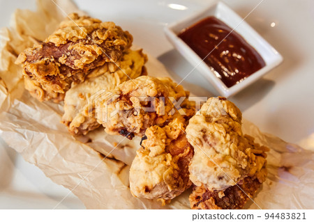 Breaded chicken wings on crumpled paper with sauce 94483821