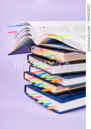 Close-up of a stack of office notepads with colorful sticky page markers with one open notepad on top 94483822