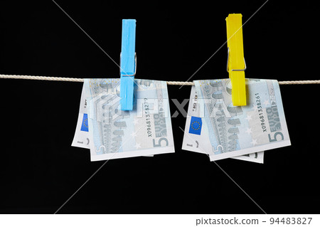 Five euro banknotes fastened with clothespins are dried on a clothesline on dark background 94483827