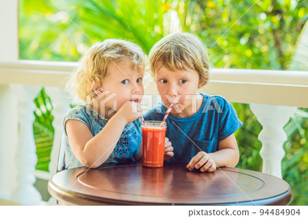Children boy and girl drink orange smoothie from papaya Children boy and girl drink orange smoothie from papaya 94484904