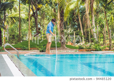 Cleaner of the swimming pool . Man in a blue shirt with cleaning equipment for swimming pools, sunny 94485120