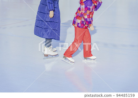 Abstract unrecognizable mother with daughter skating outdoors in skating rink. Winter activity, sport Abstract unrecognizable mother with daughter skating outdoors in skating rink. Winter activity, sport 94485159