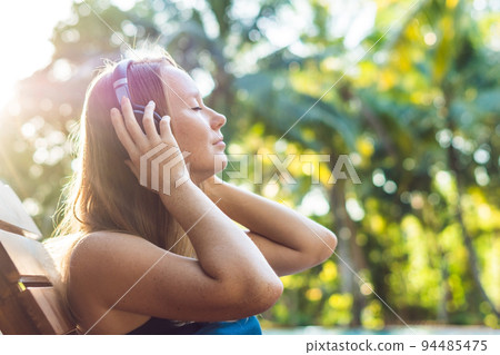 Happy smartphone woman relaxing near swimming pool listening with earbuds to streaming music. Beautiful girl using her mobile phone app 4g data to play songs while relaxing on summer luxury vacations Happy smartphone woman relaxing near swimming pool listening with earbuds to streaming music. Beautiful girl using her mobile phone app 4g data to play songs while relaxing on summer luxury vacations 94485475