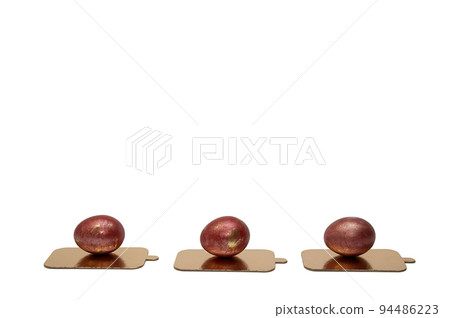 Three chicken festive Easter eggs painted with red paint lie in one line on golden stands on a large white background - side view. Three chicken festive Easter eggs painted with red paint lie in one line on golden stands on a large white background - side view. 94486223