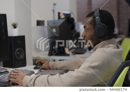 African American designer in headphones draws on tablet 3D models for games. African American designer in headphones draws on tablet 3D models for games. 94486574