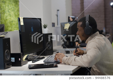 African American designer in headphones draws on tablet 3D models for games. African American designer in headphones draws on tablet 3D models for games. 94486576