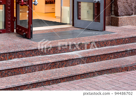 red marble staircase with granite steps to entrance door on store with glass, threshold with doormat at facade of building on retro style side view closeup, nobody. red marble staircase with granite steps to entrance door on store with glass, threshold with doormat at facade of building on retro style side view closeup, nobody. 94486702