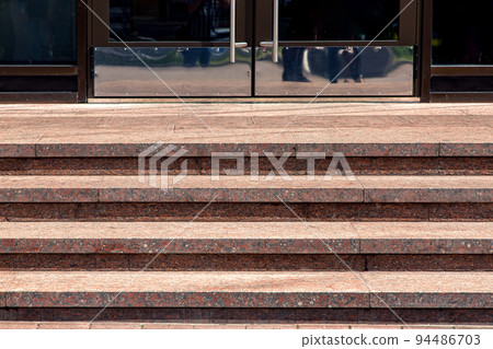 granite staircase with stone steps rise to the entrance front door with stainless steel handle on building facade architecture lit by sun close-up, front view, nobody. granite staircase with stone steps rise to the entrance front door with stainless steel handle on building facade architecture lit by sun close-up, front view, nobody. 94486703