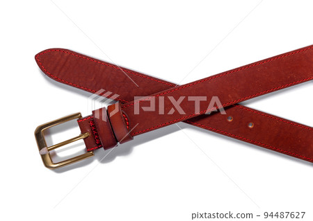 A crossed brown leather belt with a metal buckle on a white background is isolated. A crossed brown leather belt with a metal buckle on a white background is isolated. 94487627