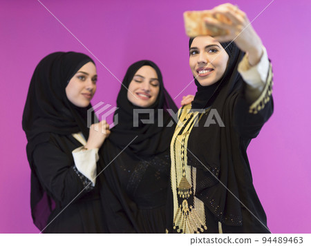 group of beautiful muslim women two of them in fashionable dress with hijab using mobile phone while taking selfie picture isolated on pink background representing modern islam fashion technology group of beautiful muslim women two of them in fashionable dress with hijab using mobile phone while taking selfie picture isolated on pink background representing modern islam fashion technology 94489463