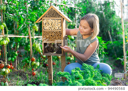Portrait of happy girl next to hotel for insects in of wooden birdhouse in garden Portrait of happy girl next to hotel for insects in of wooden birdhouse in garden 94490568