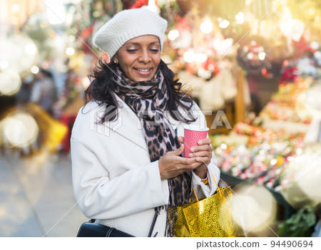 Cheerful Latina with cup of hot tea walking at Christmas street fair Cheerful Latina with cup of hot tea walking at Christmas street fair 94490694