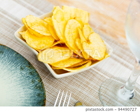 Plate of crispy deep-fried chips of thinly sliced potatoes 94490727
