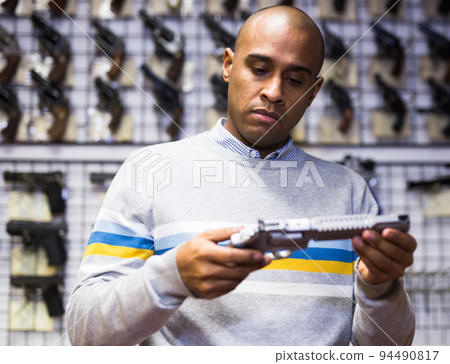 Latino choosing sporting and hunting revolvers in gunsmith shop 94490817