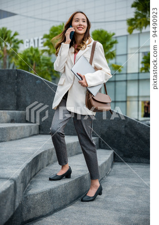 Business woman hold laptop computer talking mobile phone she hurry up walking on stairway 94490923