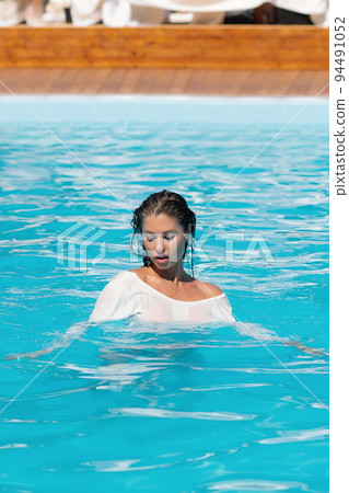 Sensual lady in wet dress standing in pool during summer vacation Sensual lady in wet dress standing in pool during summer vacation 94491052