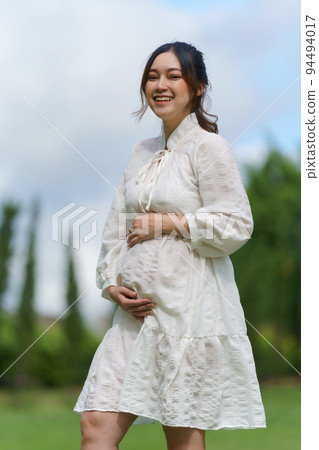 cheerful pregnant woman standing in park 94494017