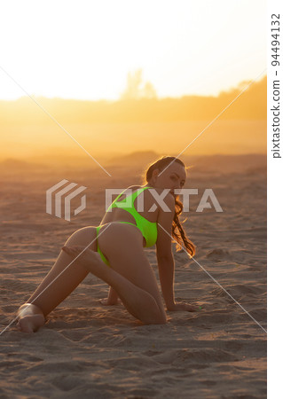 Seductive model in swimsuit kneeling on sandy beach 94494132
