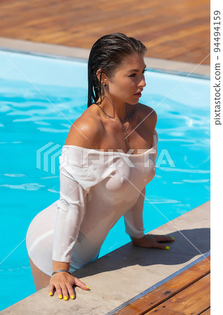 Alluring lady leaning on pool edge and looking away 94494159