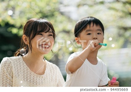 A smiling boy playing soap bubbles in the park and a mother/child-rearing image 94495669