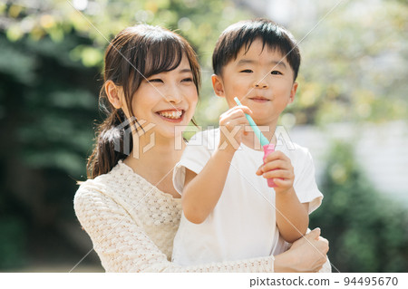 A smiling boy playing soap bubbles in the park and a mother/child-rearing image 94495670