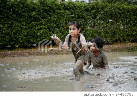 Two happy children child girl catching big frog in the large wet mud puddle on summer day. 94495793