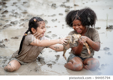 Two happy children child girl catching big frog in the large wet mud puddle on summer day. 94495794