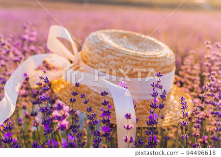 Straw hat on lavender flower field background with beautiful purple colors and bokeh lights. Blooming lavender in a field at sunset in Provence, France. Close up. Selective focus. Straw hat on lavender flower field background with beautiful purple colors and bokeh lights. Blooming lavender in a field at sunset in Provence, France. Close up. Selective focus. 94496618