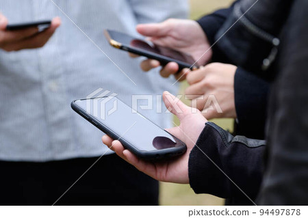 People playing smartphone games and exchanging addresses outdoors People playing smartphone games and exchanging addresses outdoors 94497878