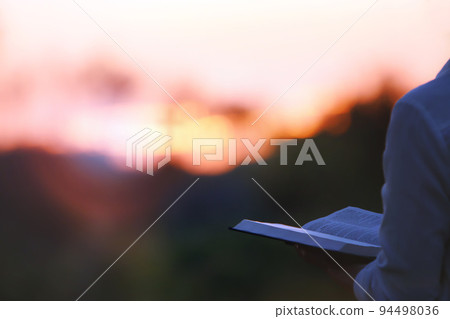 A Christian who reads, meditates and prays with the sunset scenery and the holy bible 94498036
