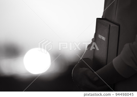 Christian silhouette hugging and praying with sunset landscape and holy bible 94498045