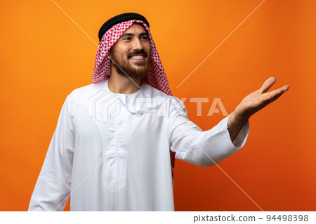 Young Arab man pointing hand to copy space on orange background Young Arab man pointing hand to copy space on orange background 94498398
