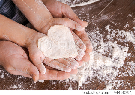 Top view father and child's hand, cut out heart shaped cookies from dough 94498794