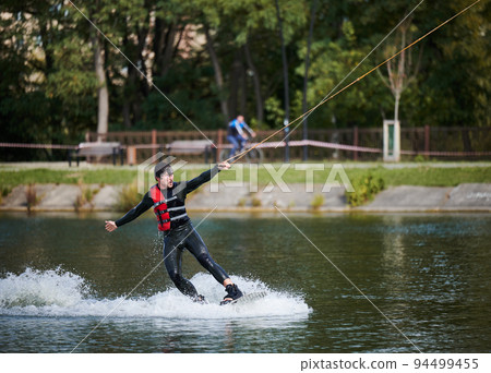 Wakeboarder surfing on lake. Young man surfer having fun wakeboarding in the cable park. Water sport, outdoor activity concept. 94499455