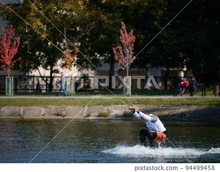 Wakeboarder surfing on lake. Young man surfer having fun wakeboarding in the cable park. Water sport, outdoor activity concept. Wakeboarder surfing on lake. Young man surfer having fun wakeboarding in the cable park. Water sport, outdoor activity concept. 94499458