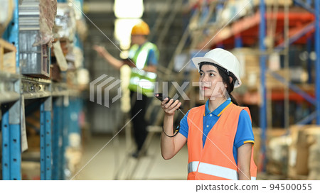 Warehouse workers in safety uniform working in warehouse full of tall shelves with goods in cardboard boxes Warehouse workers in safety uniform working in warehouse full of tall shelves with goods in cardboard boxes 94500055