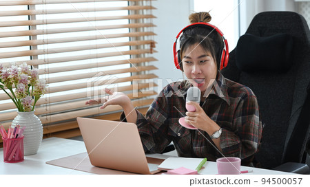 Young podcaster using a microphone and laptop computer recording audio for channel in home studio Young podcaster using a microphone and laptop computer recording audio for channel in home studio 94500057
