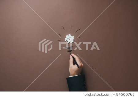 Hand of a businessman drawing a lightbulb stem to a bulb made of puzzle pieces 94500765