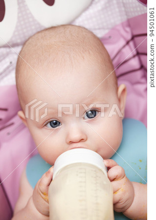 baby 6 months old sits and drinks milk from a bottle 94501061