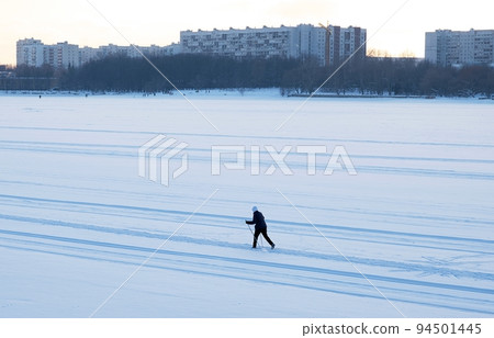 Silhouette of a skier skiing on the snow in the bed of a frozen river in the city. Silhouette of a skier skiing on the snow in the bed of a frozen river in the city. 94501445
