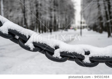 Snow-covered textured thick cast-iron chain of fencing in one of the Moscow parks in Russia in winter. 94501464