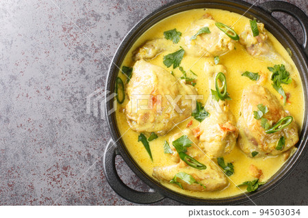 Chicken pieces stewed in coconut sauce with spices, tomato, garlic, onion and chili pepper close-up in pan on the table. horizontal top view 94503034