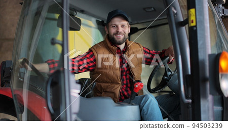 Portrait of caucasian male farmer in cap sitting in tractor with open door and smiling to camera. Agriculture farming. 94503239
