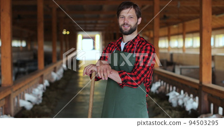 Handsome man in green apron looking at camera on goat husbandry. Formal clothes. Ecologically friendly farming. Handsome man in green apron looking at camera on goat husbandry. Formal clothes. Ecologically friendly farming. 94503295