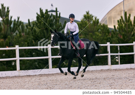 Female rider on horseback riding trot around the sandy arena in countryside, in summer day, outdoors. Dressage of horses. Horseback riding 94504485