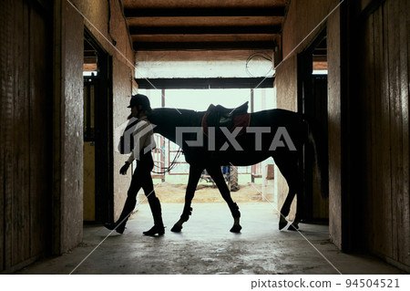 Live portrait of young girl, teen, beginner rider in sports uniform and helmet going with horse to arena. Lifestyle mood. Concept of nature, animal, care, sport Live portrait of young girl, teen, beginner rider in sports uniform and helmet going with horse to arena. Lifestyle mood. Concept of nature, animal, care, sport 94504521